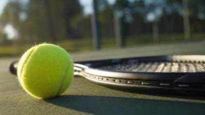 Nahaufnahme eines gelben Tennisballs neben einem Tennisschläger auf grünem Platz