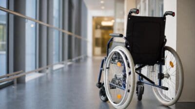 Leerer Rollstuhl steht in einem hellen Krankenhausflur mit großen Fenstern