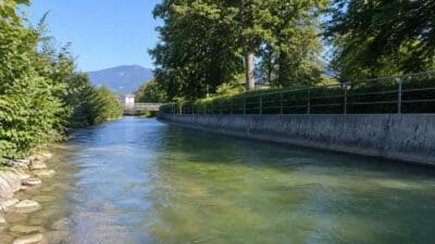Grünlich verfärbter Almkanal mit Betonmauer, Geländer und Bäumen am Ufer