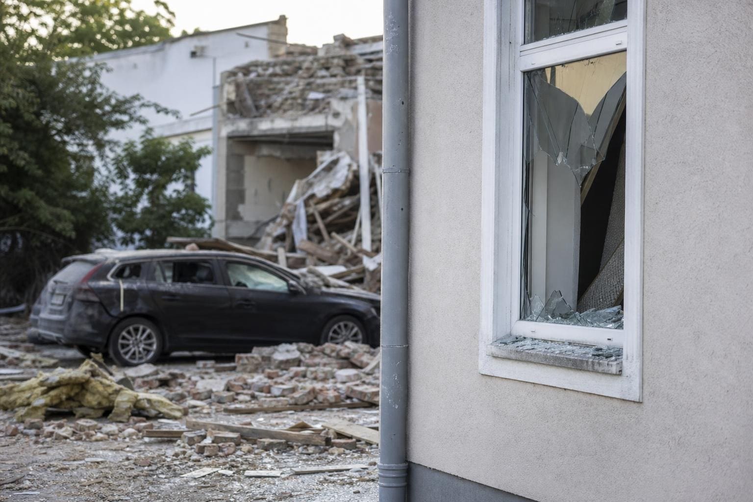 Zerstörtes Gebäude mit zerbrochenem Fenster, Trümmern und beschädigtem Auto nach Gasexplosion