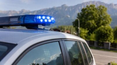 Leuchtende blaue Polizeileuchte auf dem Dach eines silbernen Einsatzwagens vor Bergen