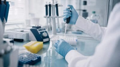 Wissenschaftlerin mit blauen Handschuhen pipettiert Flüssigkeit in ein Reagenzglas im Labor