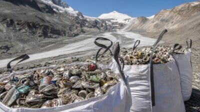Drei große weiße Säcke mit zerdrückten Aludosen vor einem Gletscher und schneebedeckten Bergen
