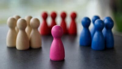 Eine pinke Spielfigur steht allein vor Gruppen aus beigen, roten und blauen Figuren.