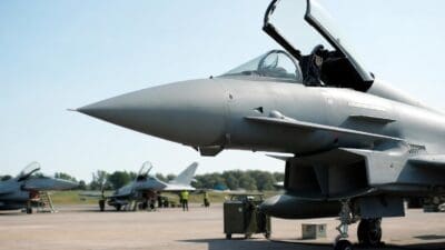 Grauer Eurofighter mit geöffneter Cockpit-Haube im Vordergrund, weitere Jets und Personal auf dem Rollfeld
