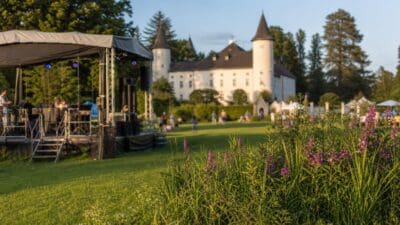 Musiker auf einer Bühne vor einem weißen Schloss auf einer Wiese