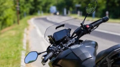 Nahaufnahme des Lenkers eines schwarzen Motorrads mit Spiegeln und Display auf einer Landstraße