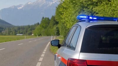 Heck eines silbernen Polizeiwagens mit blauem Blaulicht an einer Landstraße vor Bergen