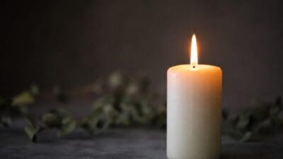Brennende weiße Kerze auf dunkler Oberfläche vor unscharfem Grünzeug