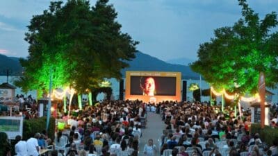 Zuschauer auf weißen Stühlen vor großer Leinwand beim Freiluftkino Movie at the Lake in Klagenfurt