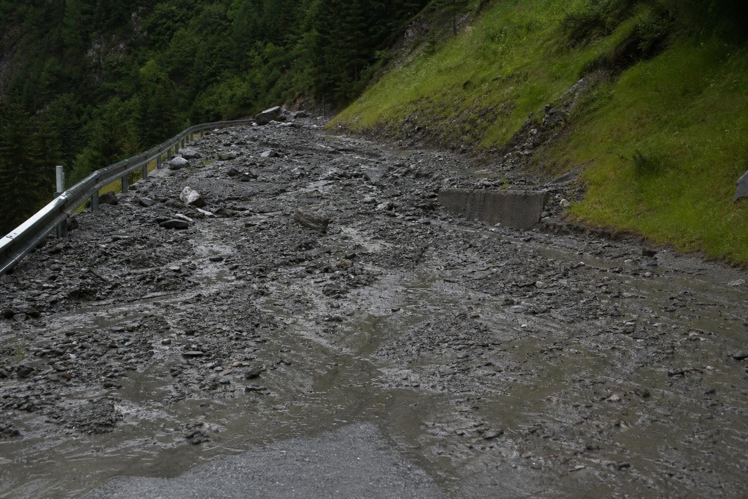 Schlamm und Geröll bedecken eine Bergstraße mit Leitplanke im Ötztal