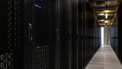 Langer Gang in einem Rechenzentrum mit schwarzen Server-Racks und leuchtenden Kontrollleuchten