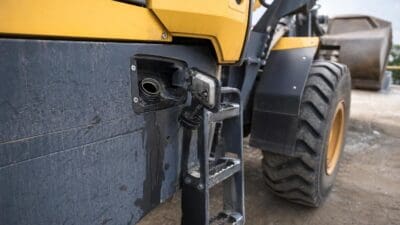 Nahaufnahme des geöffneten Tankstutzens einer gelb schwarzen Baumaschine mit austretender Flüssigkeit