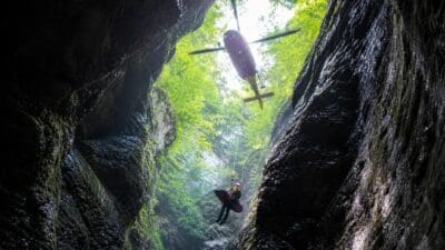 Rettungskraft wird mit Trage von einem Hubschrauber aus einer engen Schlucht gehoben