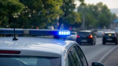 Weißes Polizeifahrzeug mit leuchtendem blauen Blaulichtbalken auf einer Straße