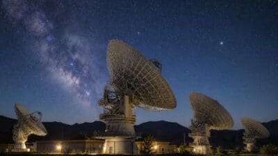 Mehrere große Radioteleskope mit Parabolantennen unter einem sternenreichen Nachthimmel mit sichtbarer Milchstraße