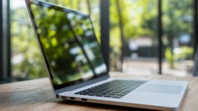 Silberner Laptop steht aufgeklappt auf einem Holztisch vor unscharfem grünem Hintergrund