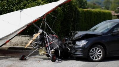 Beschädigter Hängegleiter mit weißem Segel liegt nach Kollision auf schwarzem Pkw