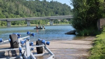 Einsatzkräfte in einem Schlauchboot auf der Drau bei einer Brücke und einem Bootstrailer am Ufer