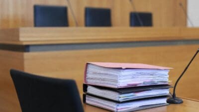 Stapel aus rosa und schwarzen Aktenordnern auf einem Tisch in einem Gerichtssaal mit Mikrofonen