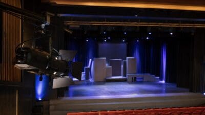 Bühne mit weißen Kulissen und blauer Beleuchtung im leeren Theatersaal mit roten Sitzreihen
