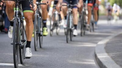 Nahaufnahme der Beine und Räder von Rennradfahrern auf einer asphaltierten Straße.
