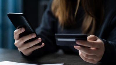 Junge Frau hält Smartphone in der einen und Kreditkarte in der anderen Hand