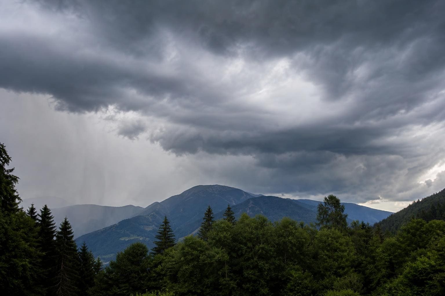 Dunkle Gewitterwolken über bewaldeten Bergen und dichten Nadelbäumen