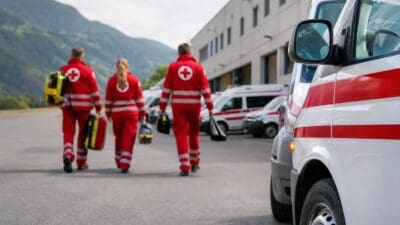 Rettungskräfte des Roten Kreuzes in roten Uniformen gehen mit Taschen zu Rettungswagen