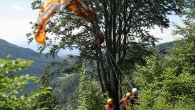Ein orangefarbener Paragleiter hängt in einem Baum während Rettungskräfte ihn bergen.