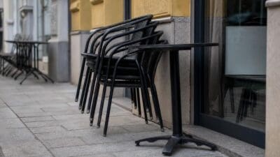 Gestapelte schwarze Stühle und ein Tisch vor einem gelben Gebäude auf dem Gehsteig