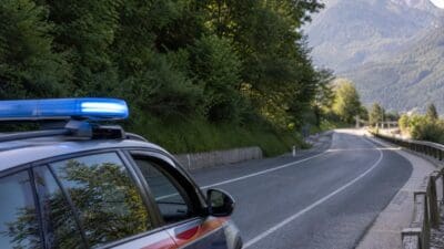 Polizeifahrzeug mit blauem Blaulicht steht am Rand einer kurvigen Autobahn in bergiger Landschaft
