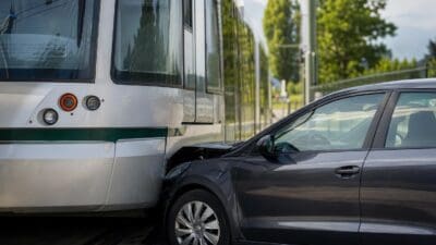 Grauer Pkw mit eingedrückter Front stoßt seitlich an weiße Straßenbahn mit grünem Streifen