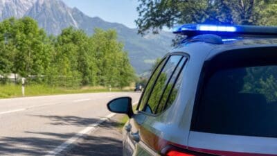 Heck eines Polizeifahrzeugs mit blauem Blaulicht auf einer Landstraße vor Bergen