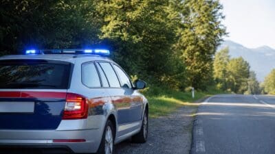 Heckansicht eines silbernen Polizeiwagens mit Blaulicht am Rand einer Landstraße