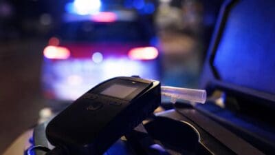 Schwarzes Atemalkoholmessgerät mit Mundstück vor unscharfem Polizeiauto mit Blaulicht bei Nacht