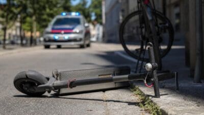 Ein E-Scooter liegt auf dem Boden neben einem Fahrrad vor einem Polizeiauto mit Blaulicht.