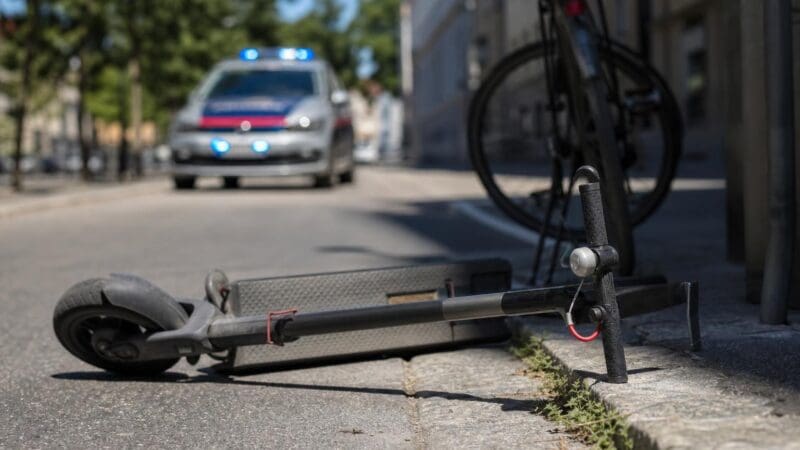 Ein E-Scooter liegt auf dem Boden neben einem Fahrrad vor einem Polizeiauto mit Blaulicht.
