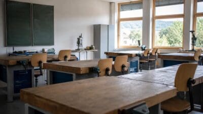Leerer Werkraum mit Holz-Werkbänken, Stühlen, Werkzeugen und Tafeln vor großen Fenstern