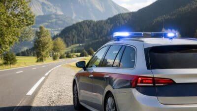Silbernes Polizeifahrzeug mit aktiviertem Blaulicht am Rand einer Straße in den Bergen