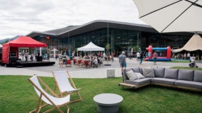 Eventgelände vor einem modernen Glasgebäude mit Bühne, Zelten, Hüpfburg und vielen Besuchern in Seefeld