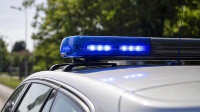 Blaues Blaulicht auf dem Dach eines weißen Polizeifahrzeugs mit grünen Bäumen im Hintergrund