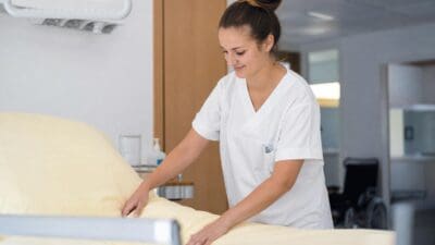 Eine Pflegekraft in weißer Uniform richtet ein Krankenbett her.