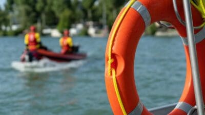 Oranger Rettungsring mit gelbem Seil im Vordergrund, dahinter ein Boot mit zwei Wasserrettern