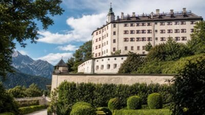 Das Schloss Ambras mit vielen Fenstern und roten Läden vor einer Bergkulisse.