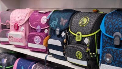 Mehrere bunte Schultaschen mit Reflektoren und Anhängern auf einem weißen Regal