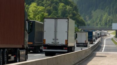 Mehrere Lastwagen fahren hintereinander auf einer kurvigen Autobahn in einer bewaldeten Hügellandschaft.