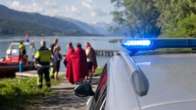 Einsatzfahrzeug mit Blaulicht und gerettete Personen in roten Decken am Seeufer