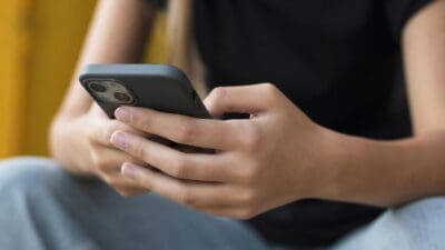 Nahaufnahme von Händen, die ein Smartphone mit grauer Hülle halten.