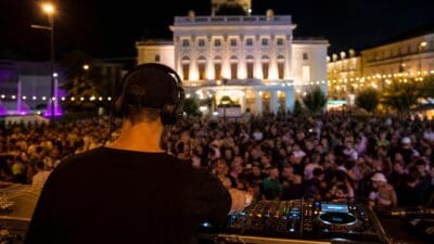 DJ mit Kopfhörern bedient Mischpult vor großem Publikum auf dem Neuen Platz in Klagenfurt bei Nacht